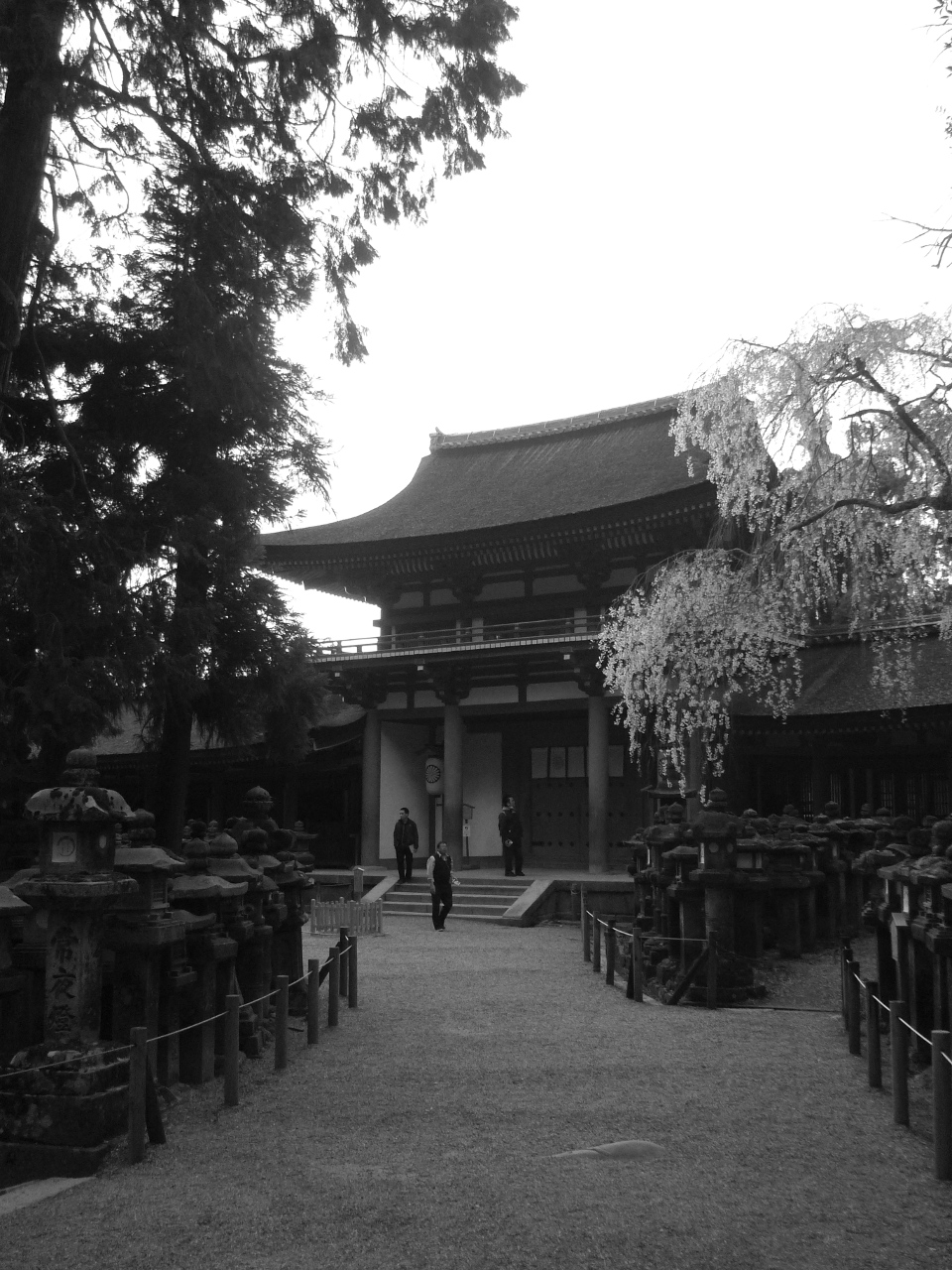 Trois hommes devant l'entrée d'un temple et devant le jardin de lanternes de pierre.