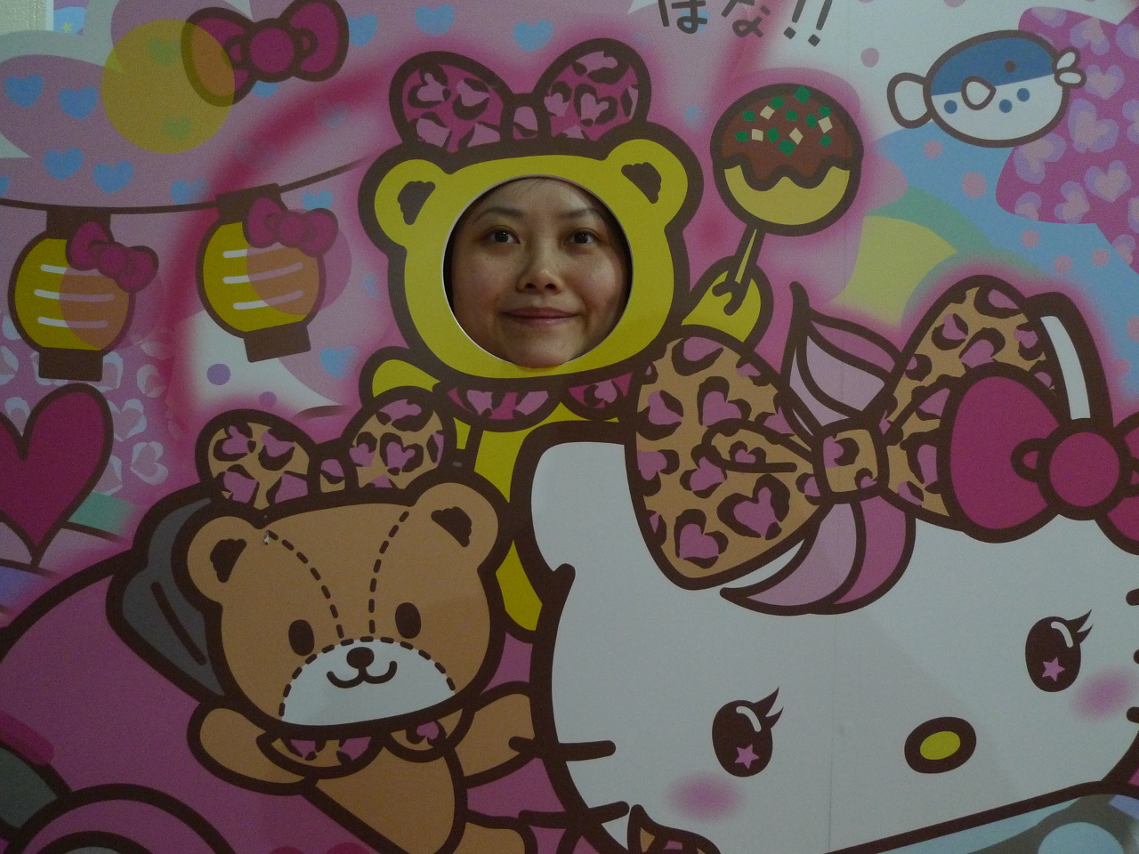 Une jeune femme pose, le visage dans un mur décoré de motifs Hello Kitty